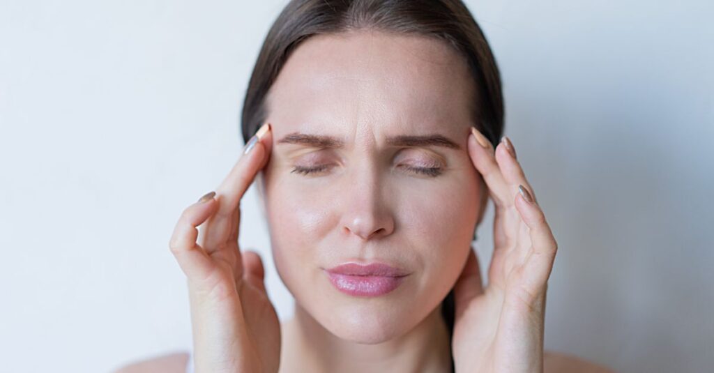 Woman holding her temples in pain, showing signs of a hormonal headache or migraine during perimenopause